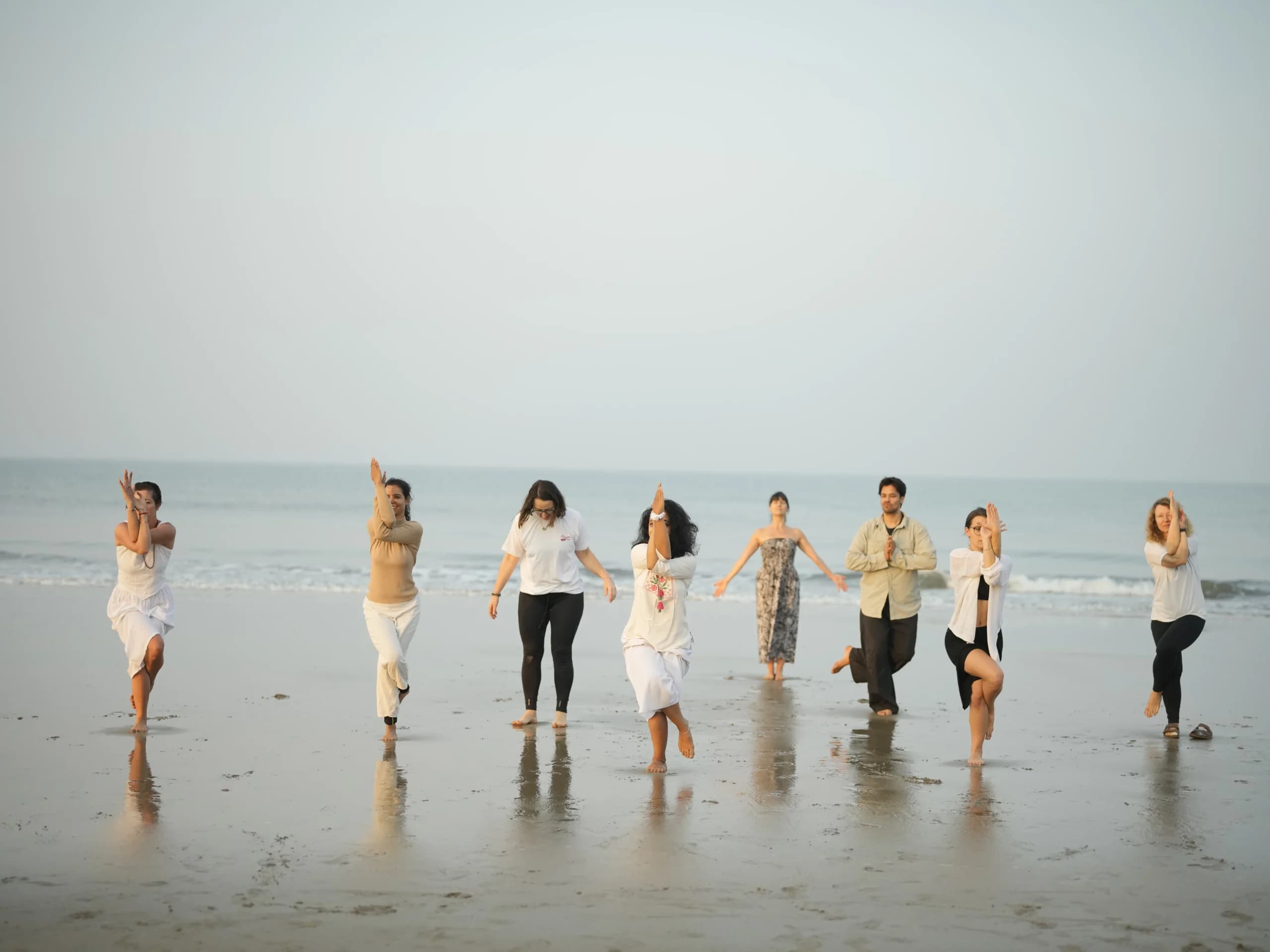 International students holding eagle-arm balance poses by the sea during yoga teacher training in Goa