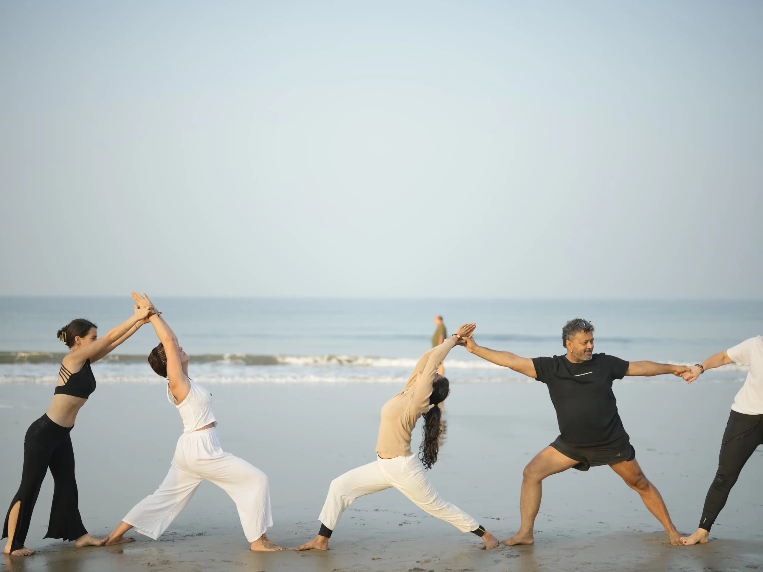 Students in a line of Warrior poses on the shoreline at Arambol Beach during Alpesh Yoga teacher training
