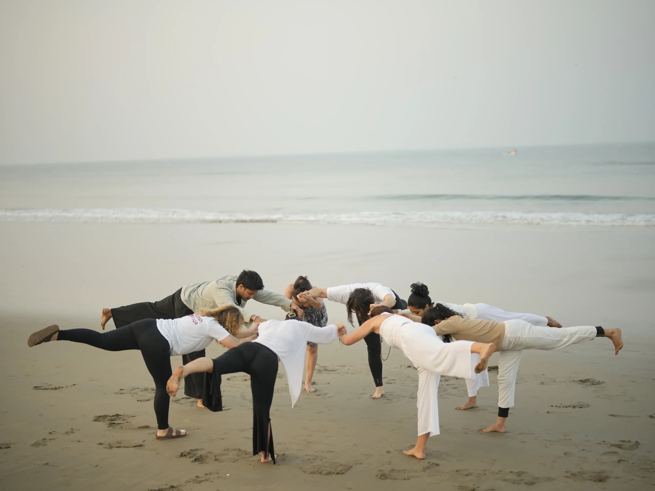 Yoga teacher training students balancing together in a Warrior III circle on the beach in Goa