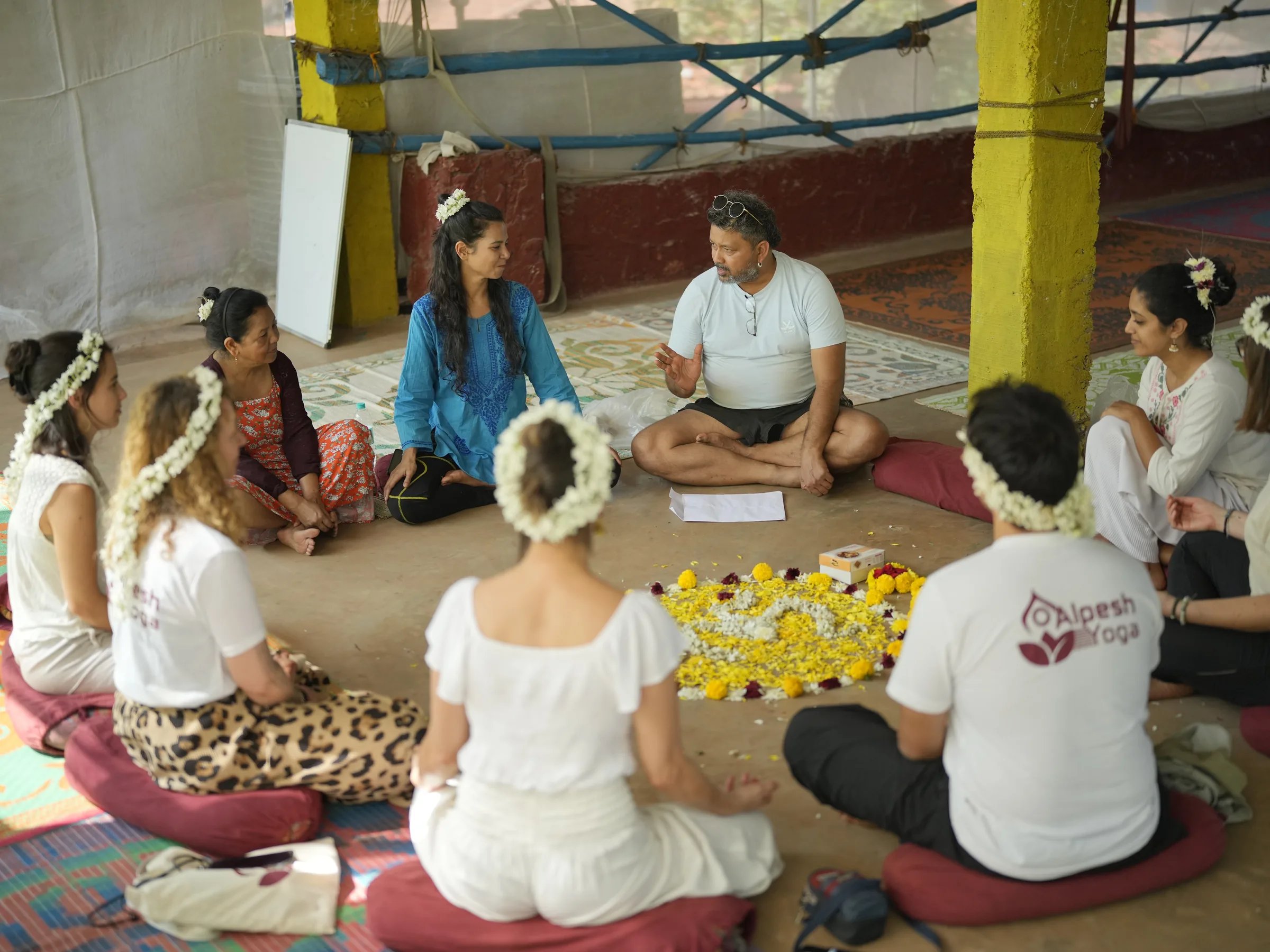Alpesh Patwari leading an opening ceremony with students seated in a circle around a marigold mandala at the Arambol shala