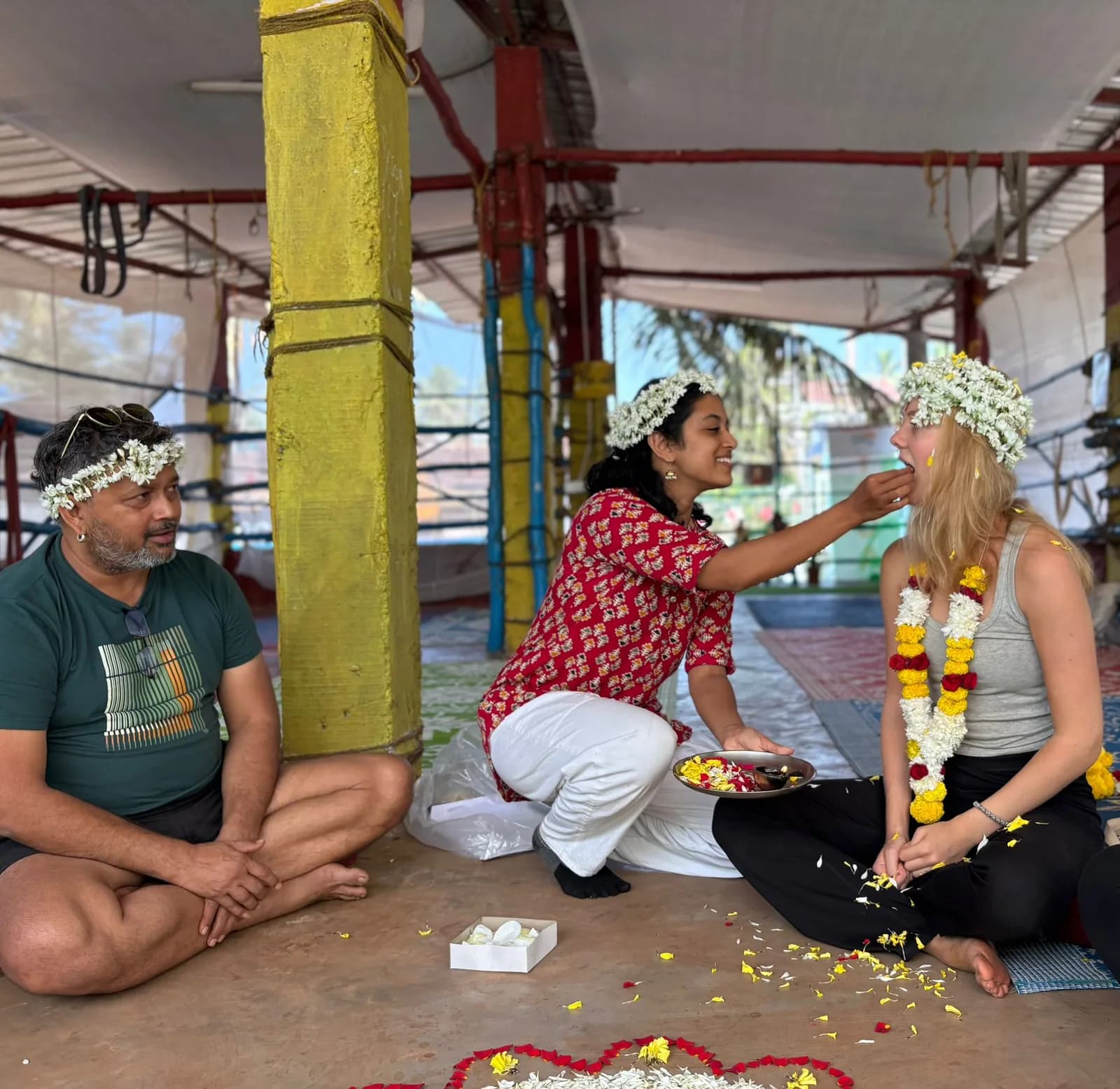 Teacher applying a tilak to a student wearing marigold garlands during an outdoor ceremony at the Arambol yoga shala