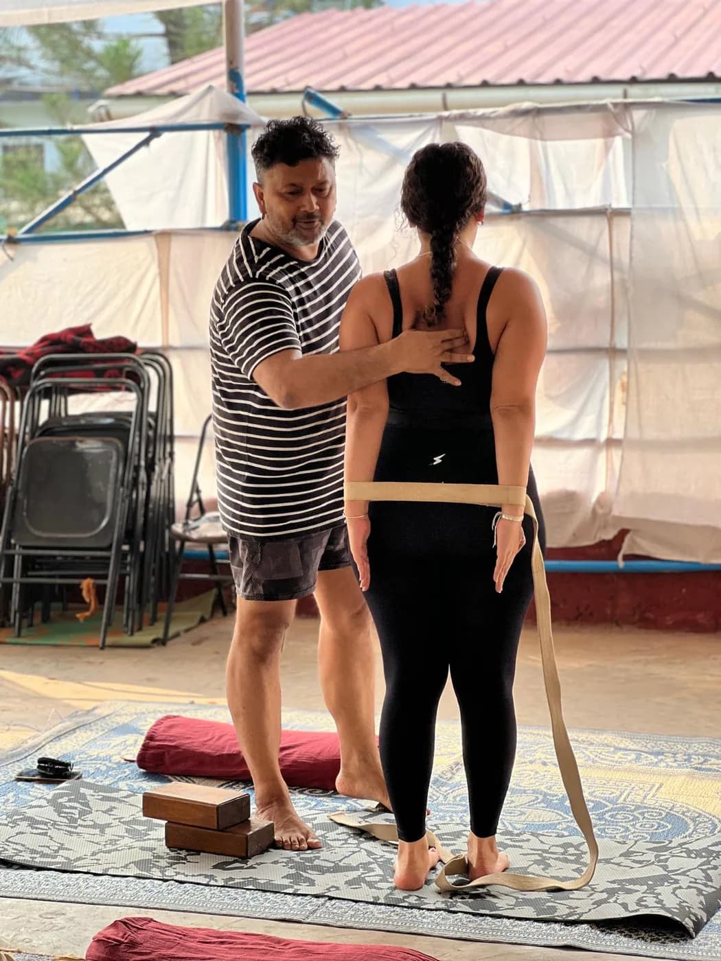 Teacher using a yoga belt to correct a student’s shoulder alignment during an alignment class