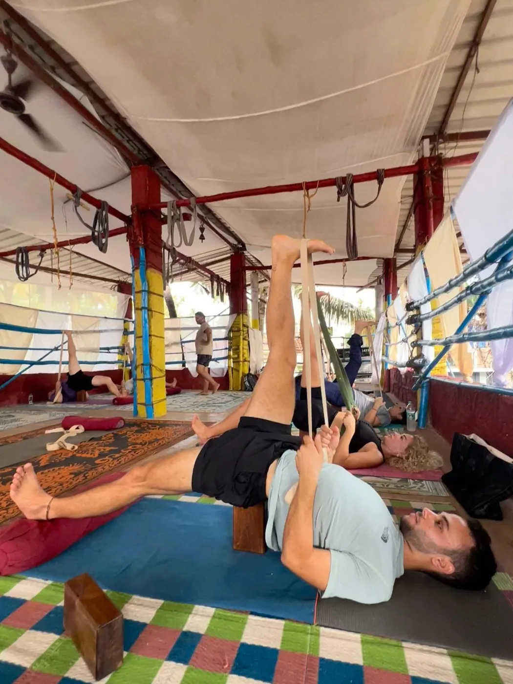 Student using a yoga belt for a supine hamstring stretch during props-based alignment practice