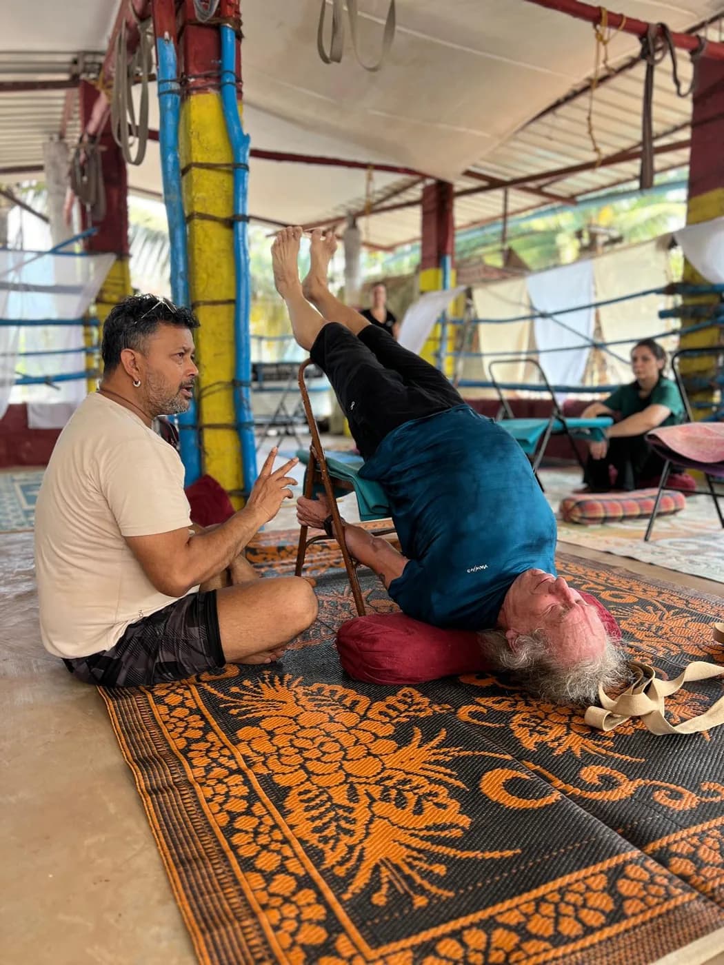 Teacher guiding an older student through a chair-supported shoulderstand on a bolster