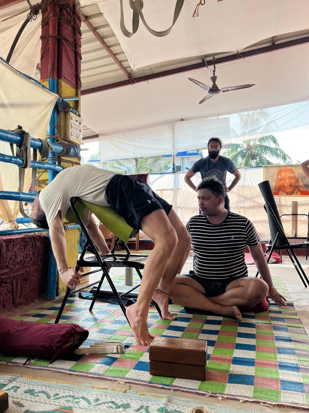 Student practising a chair-supported forward bend with a teacher watching the alignment