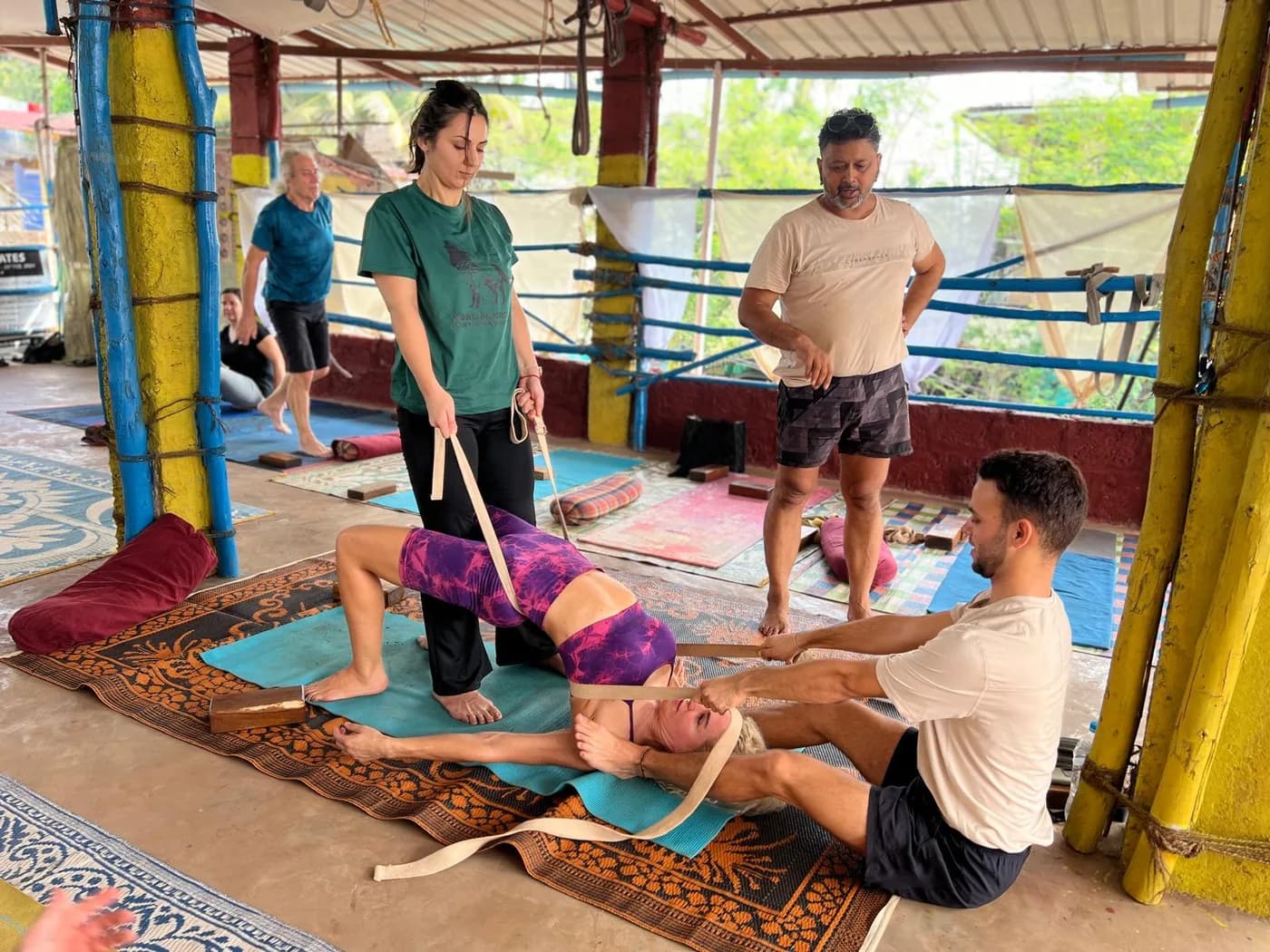 Two trainees supporting a classmate with yoga belts in a backbend while Alpesh Patwari supervises