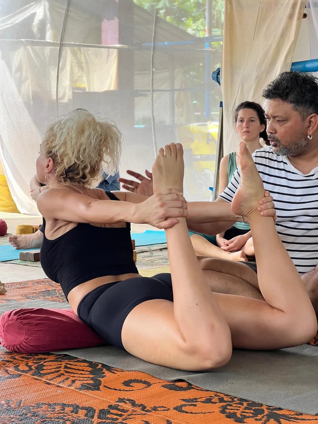 Teacher giving a hands-on adjustment to a student’s extended leg in a seated forward stretch