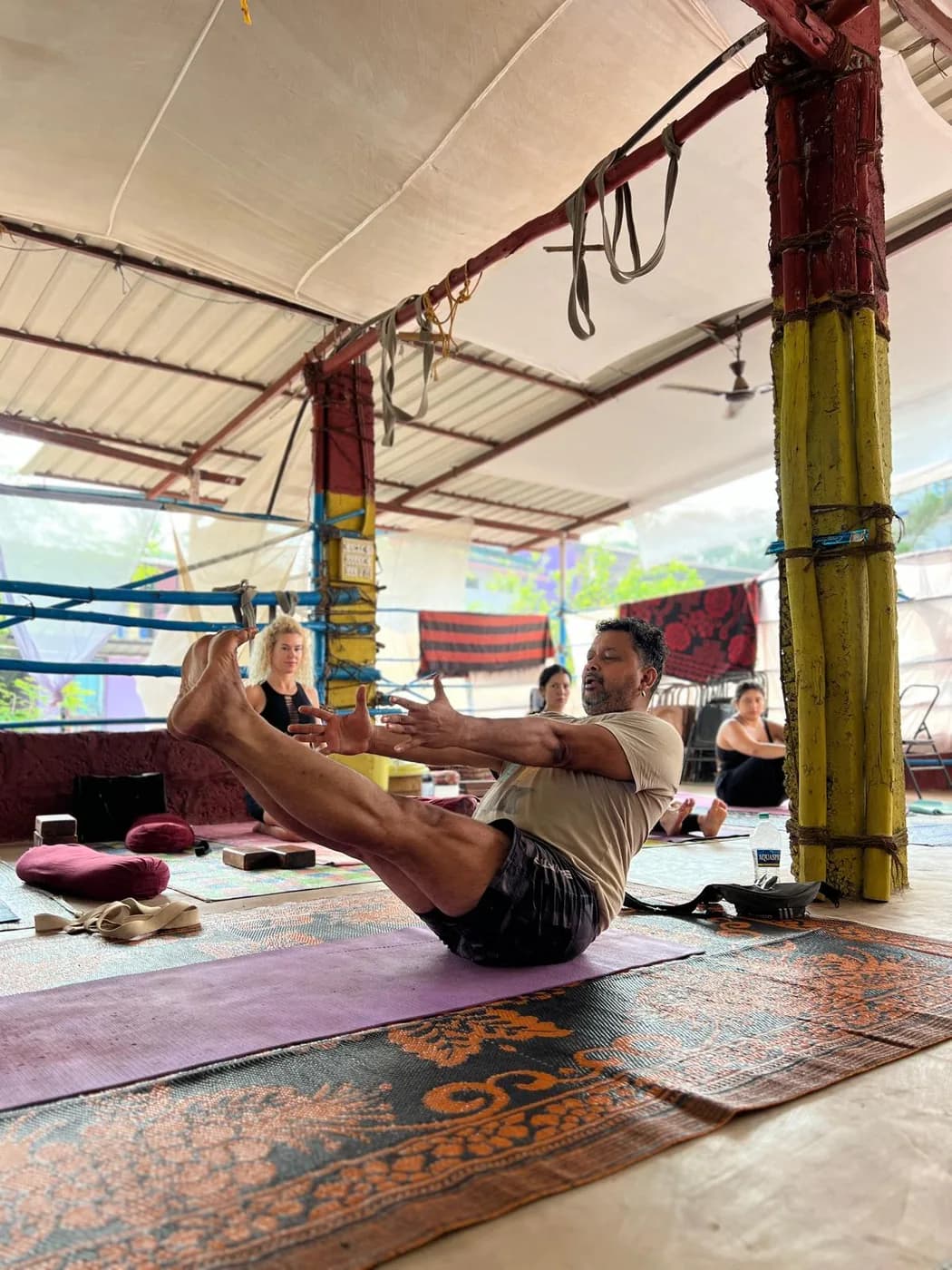 Alpesh Patwari demonstrating Navasana, the boat pose, to students seated around him