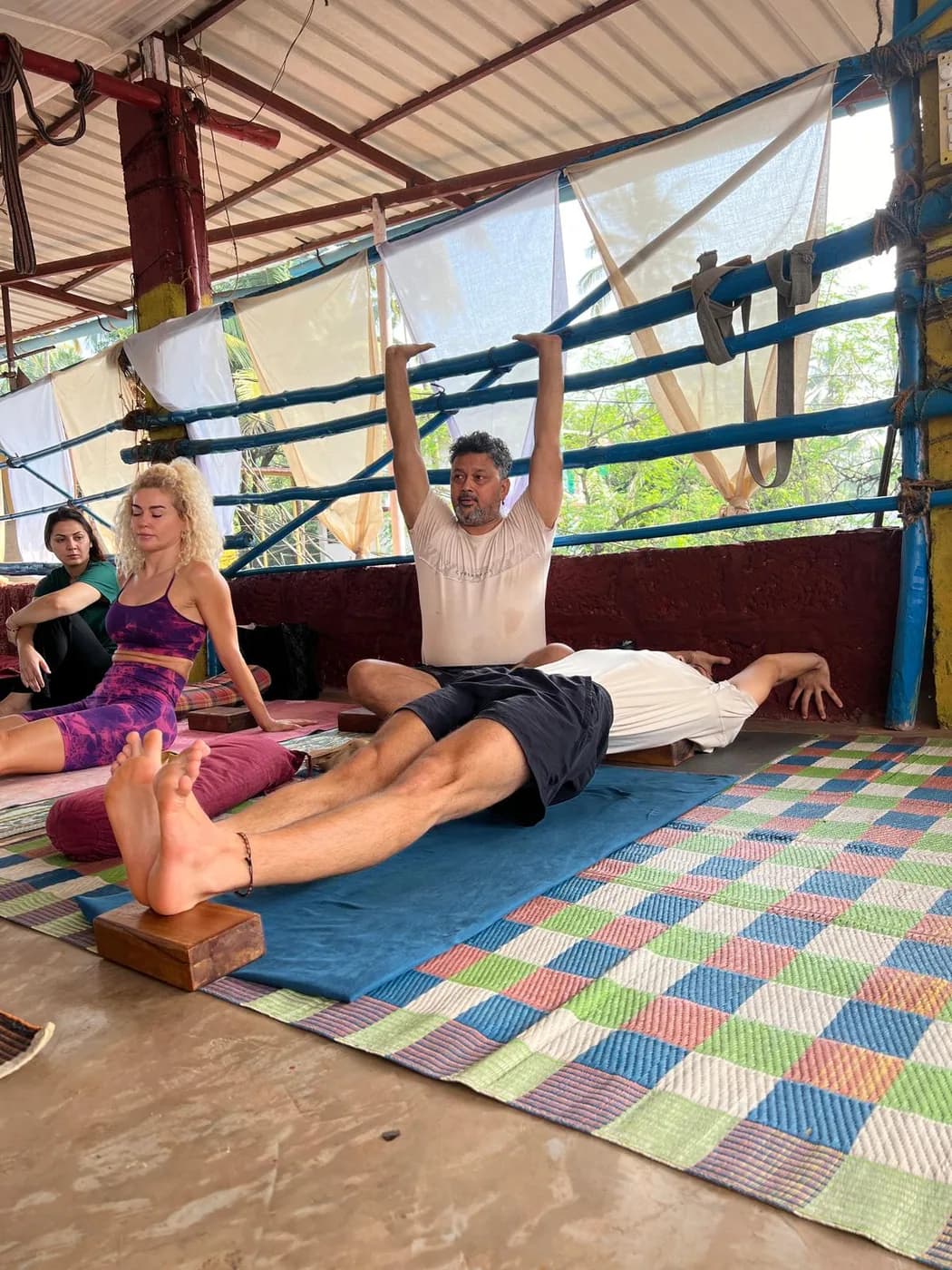 Teacher demonstrating a supine stretch to yoga teacher training students seated around him